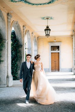 Gülümseyen yeni evliler eski terasta yeşil sarmaşıklarla çevrili kolonlarla sarılıp yürüyorlar. Como Gölü, İtalya