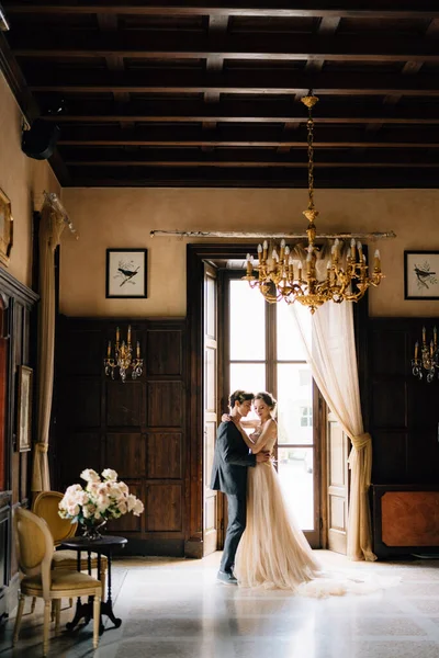 Groom está dançando com a noiva no quarto em frente à mesa com um buquê de rosas em uma antiga villa. Lago de Como — Fotografia de Stock