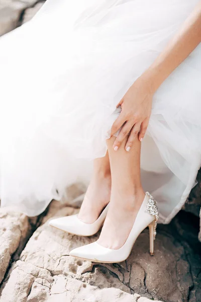 Gelin elbisesinin zeminini kaldırdı, beyaz topuklu ayakkabılarını taştan bir arka plana gösterdi. — Stok fotoğraf