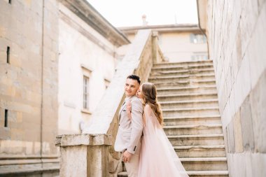 Gelin gülen damadı arkadan kucaklıyor. Yeni evliler, İtalya 'nın Bergamo kentindeki eski bir binanın merdivenlerinde dururlar.