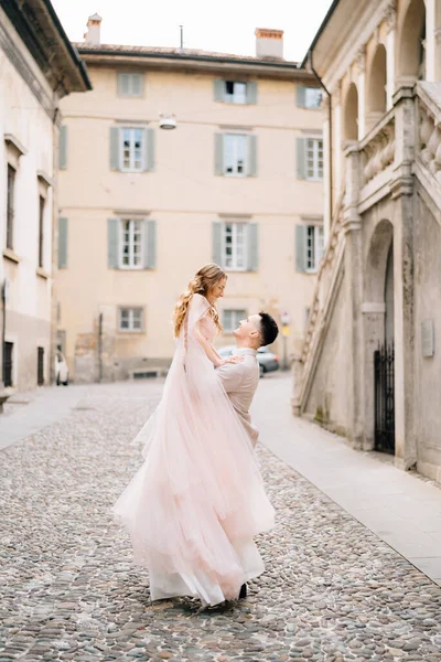 Грим тримає наречену на руках, стоячи на бруківці біля старого будинку в Бергамо (Італія). — стокове фото