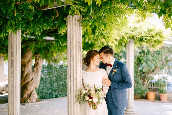 Mariée souriante étreint les épaules des mariées sur le fond de colonnes dans un jardin vert — Photo