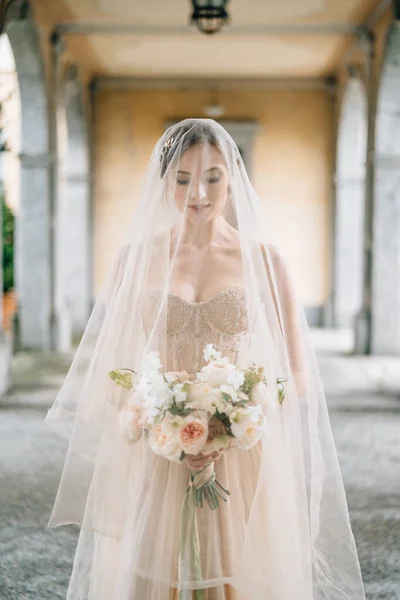 Pengantin dalam gaun pengantin dan kerudung dengan buket berdiri dengan matanya tertunduk pada teras tua dengan kolom. Danau Como — Stok Foto