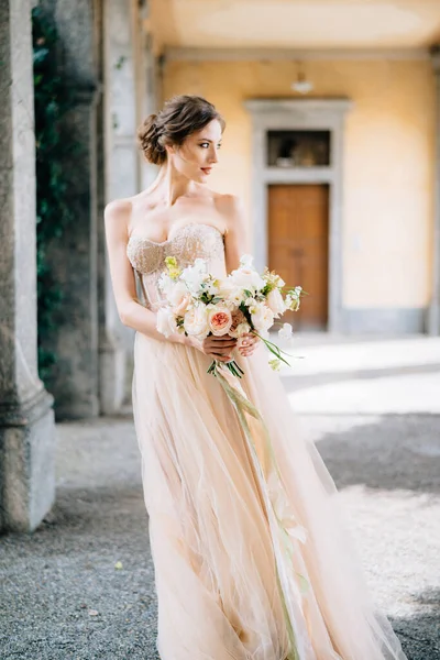 Pengantin dalam gaun yang indah dengan karangan bunga merah muda berdiri di aula berkubah dengan kepala berbalik. Danau Como, Italia — Stok Foto