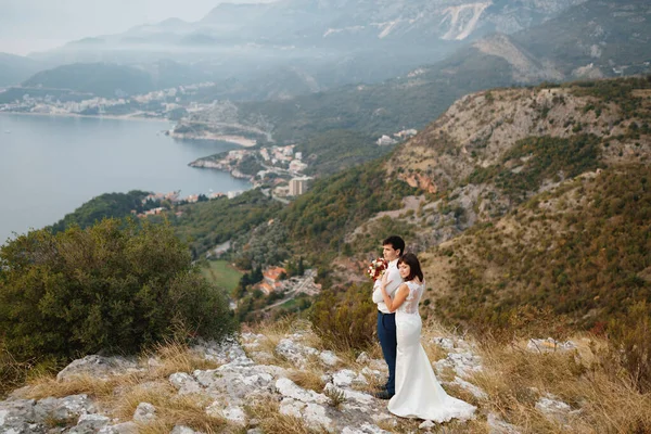 Recém-casados abraçar no fundo de um panorama da cidade de Budva, montanhas e do mar — Fotografia de Stock