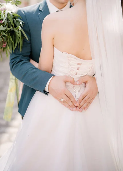 A vőlegény a kezét egy szív alakjában tartja a menyasszony hátán, fehér ruhában, megölelve őt. — Stock Fotó