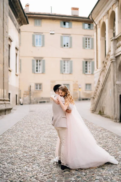 Novio abrazos novia mientras de pie en las adoquines cerca del antiguo edificio en Bérgamo, Italia —  Fotos de Stock