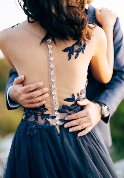 Жених в синем костюме обнимает невесту в синем платье за талию. Закрывай. Вид сзади