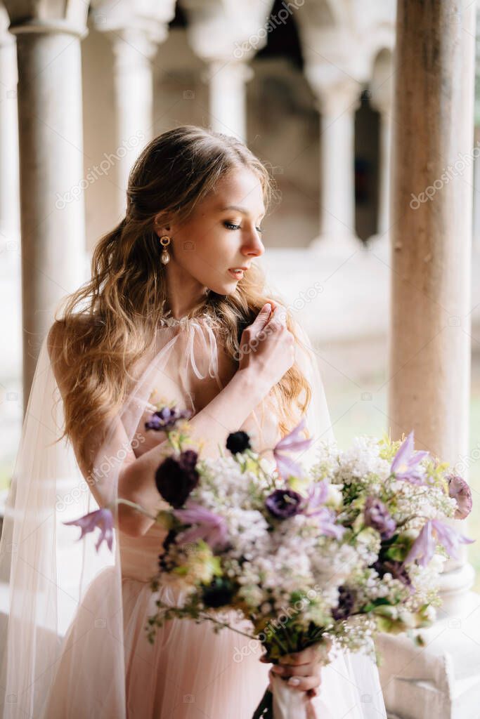 Bride in a beautiful pink dress holds a bouquet of wildflowers in her hand against the background of an old building in Lake Como