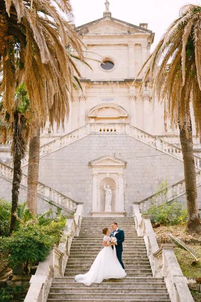 Bruden och brudgummen står kramas på trappan till Födelsekyrkan av Jungfru Maria kyrka i Prcanj — Stockfoto