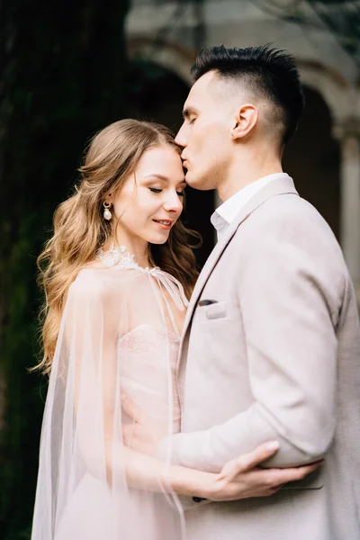 Groom embrasse le front de la mariée souriante dans une belle robe rose — Photo