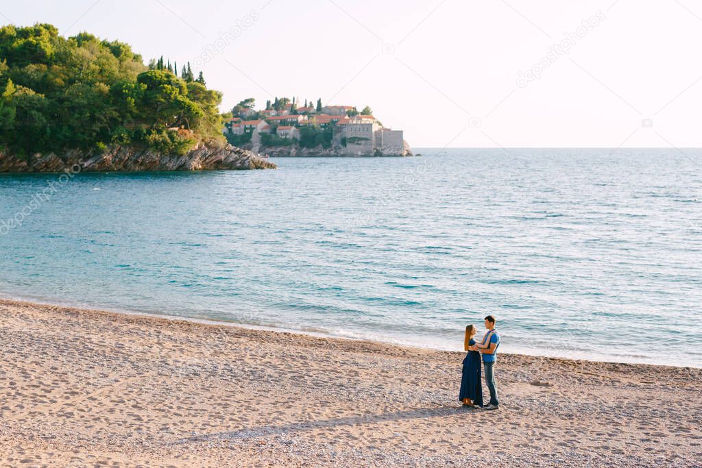 Man hugs pregnant woman against the backdrop of the panorama of Sveti Stefan island and an old villa Milocer