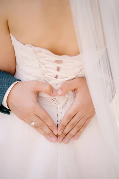 Ženich drží ruce ve tvaru srdce na zádech nevěsty v bílých šatech — Stock fotografie