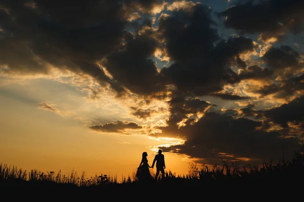 Silhouetten van man en vrouw die over de vlakte wandelen op de achtergrond van een prachtige zonsondergang hemel — Stockfoto