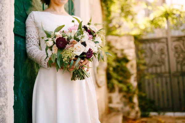 Noiva segura em suas mãos um lindo buquê de flores encostadas à porta verde do edifício — Fotografia de Stock
