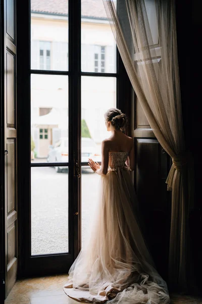 新娘站在一座旧别墅的大窗前，朝院子里看去。科摩湖背景色 — 图库照片