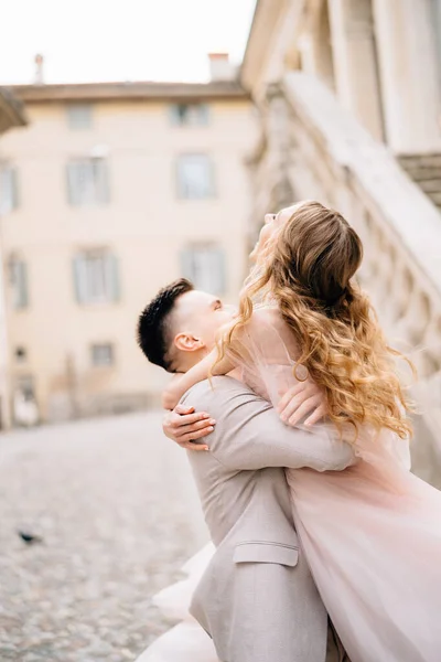 Groom tient la mariée dans ses bras sur le fond d'un vieux bâtiment à Bergame, en Italie — Photo