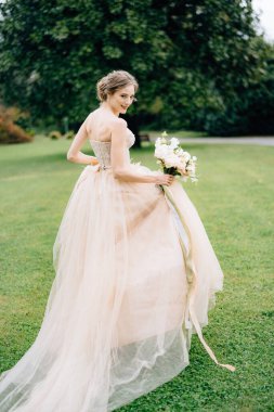 Gelin arkasını dönmüş pembe bir elbiseyle yeşil bir parkın arka planına bir buket çiçekle bakıyor. Como Gölü. Kapat.