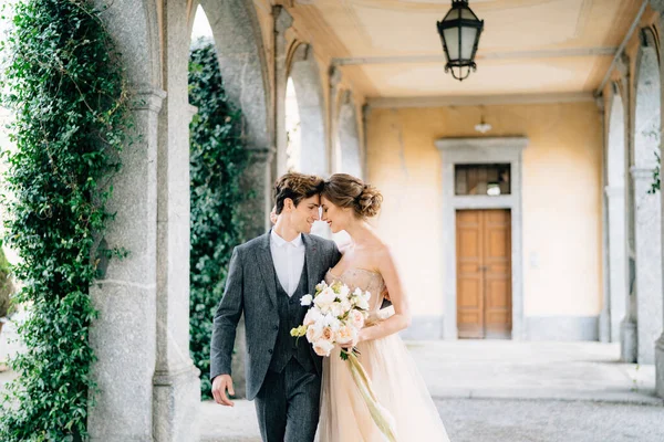 Usmívající se novomanželé se objímají při procházce po terase se sloupy na pozadí zeleně. Lake Como — Stock fotografie