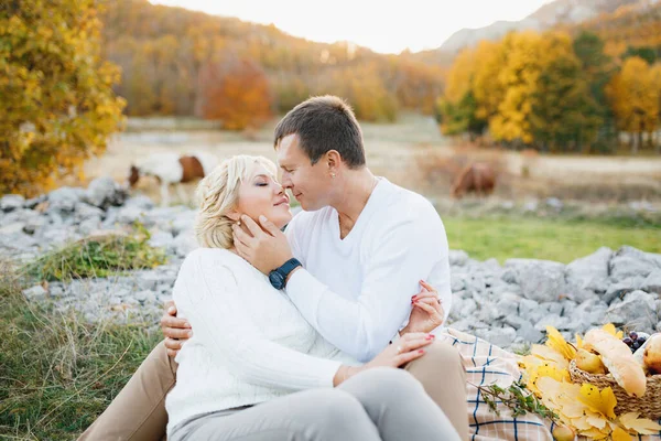 Couple embrasser assis sur une couverture sur le fond de chevaux broutant dans la forêt d'automne — Photo