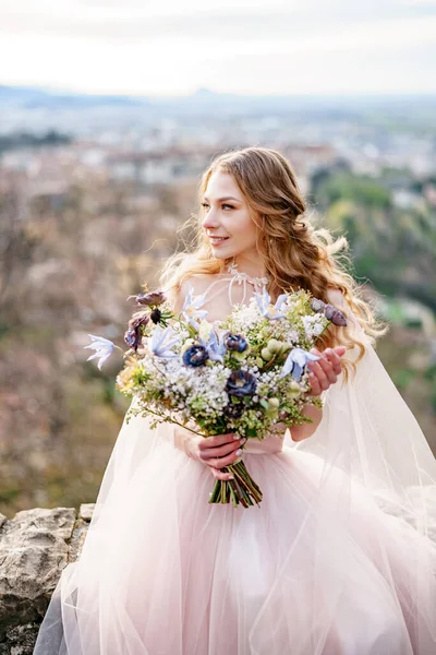 Pengantin wanita tersenyum dalam gaun pengantin merah muda yang indah terlihat ke samping. Pengantin memegang karangan bunga liar di tangannya. Bergamo, Italia — Stok Foto