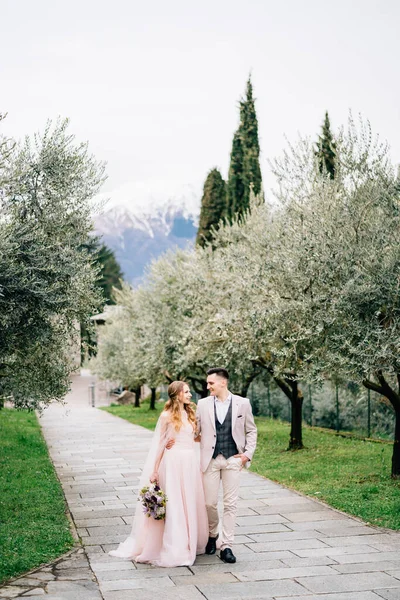 Les jeunes mariés marchent sur un sentier dans une oliveraie en fleurs dans le lac de Côme, Italie — Photo