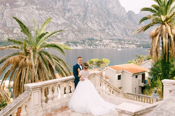 Bruden och brudgummen står och kramas i trappan i gamla stan, bakom dem är vackra hamnen — Stockfoto