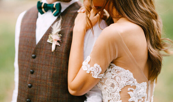 Красивая невеста в белом вышитом платье обнимает плечо жениха. Половинный портрет