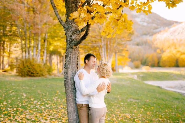 Hombre abraza a mujer por los hombros cerca de un árbol en el bosque de otoño —  Fotos de Stock