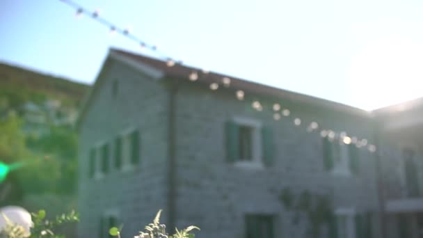 Tavolo a un banchetto di nozze con candele in barattoli di vetro e mazzi di fiori nel cortile di una villa decorata con ghirlande di lampadine — Video Stock