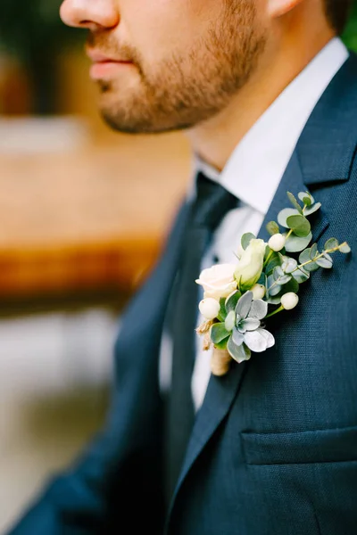 Un homme non rasé vêtu d'une veste bleue, chemise blanche, cravate et avec une boutonnière de petites roses et écheveria — Photo