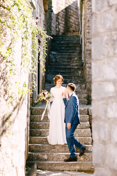 Smiling newlyweds descend the steps. Groom gave his hand to lovely bride with a beautiful bouquet — Stock Photo, Image