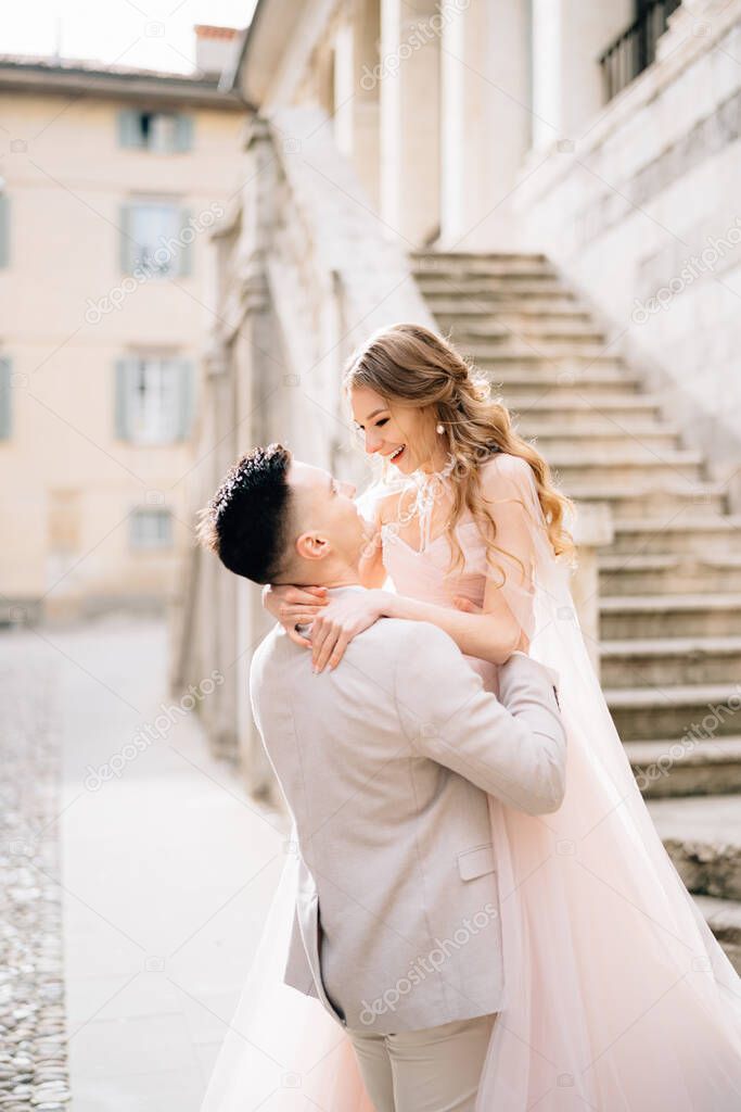 Groom holds bride in his arms near the steps of an old building in Bergamo, Italy. Close up