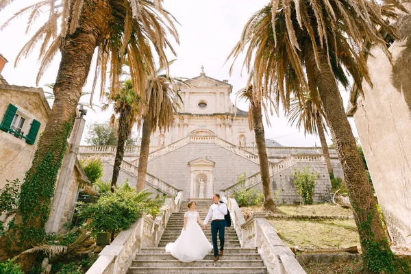 Bruden och brudgummen går ner för trapporna i Födelsekyrkan av Jungfru Maria kyrka i Prcanj och hålla händer — Stockfoto