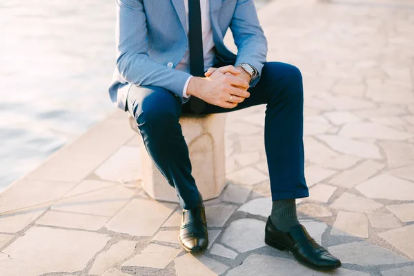 Half-portrait of man in a grey suit sitting on the embankment near the water — Stock Photo, Image