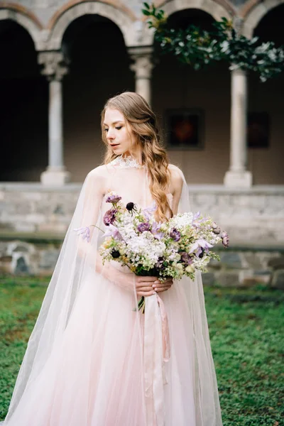 Bruid in een prachtige jurk met een boeket bloemen in een groene tuin tegen de achtergrond van een oud gebouw aan het Comomeer. Sluiten. — Stockfoto