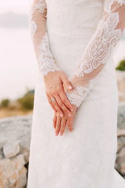 La novia en vestido con mangas de encaje dobló sus manos con un anillo de bodas en su dedo, de cerca — Foto de Stock