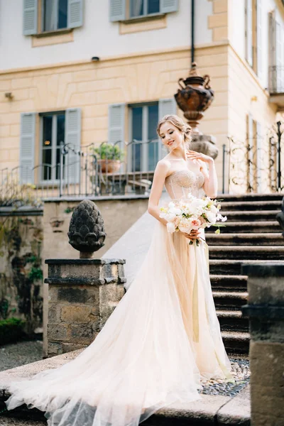 Novia sonriente en un vestido rosa con un ramo de flores se encuentra de lado en los escalones de una antigua villa. Lago de Como, Italia —  Fotos de Stock