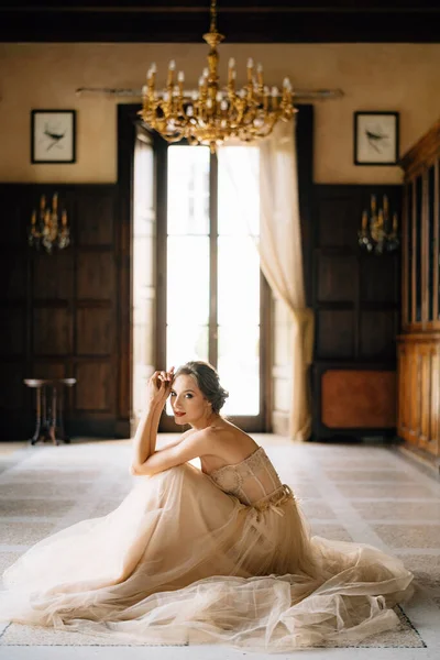 穿着漂亮衣服的新娘坐在一幢旧别墅的大窗户对面房间的地板上。科莫湖 — 图库照片