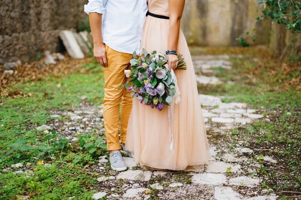 Demi-portrait de marié embrassant mariée dans une belle robe avec un bouquet dans ses mains sur le fond d'un mur de pierre — Photo