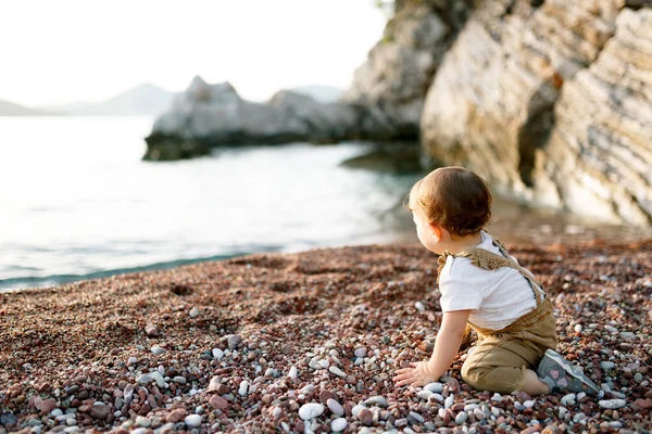 어린 소년은 바닷가에 있는 조약돌 해변에 앉아서저 멀리를바라봅니다 — 스톡 사진