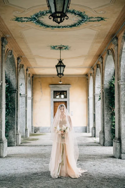 Pengantin dalam gaun pengantin dan kerudung dengan buket berjalan di sepanjang teras tua dengan kolom. Danau Como — Stok Foto