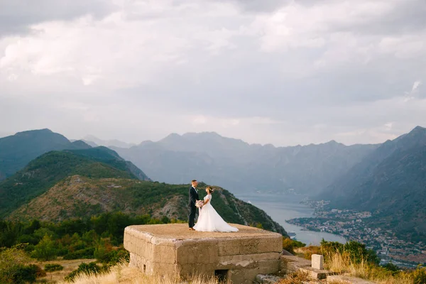 A noiva e o noivo dão as mãos no telhado do forte Gorazda, atrás deles uma vista da Baía de Kotor — Fotografia de Stock