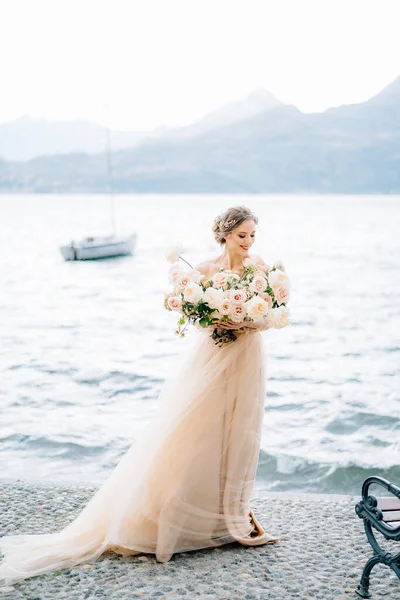 Pengantin dengan karangan bunga berdiri di tepi Danau Como dengan latar belakang kapal pesiar dan pegunungan — Stok Foto