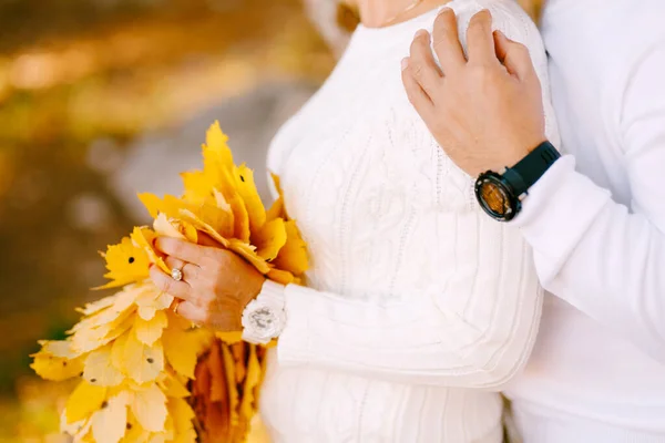 Man hugs woman against the background of an autumn forest. Woman holding a bouquet of yellow leaves