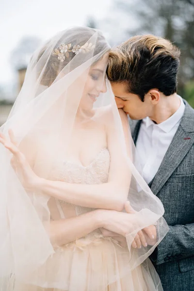El novio abraza a la novia sonriente con un velo por detrás y la besa en el hombro. Lago de Como, Italia —  Fotos de Stock