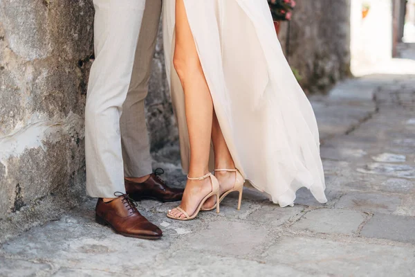 Πόδια του γαμπρού και της νύφης αγκαλιάζουν κοντά στον πέτρινο τοίχο στο στενό δρόμο του παλιού γορόλου, κοντινό πλάνο — Φωτογραφία Αρχείου