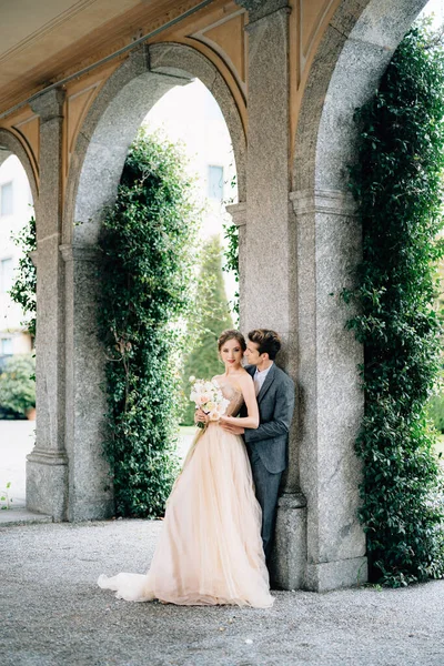 Los recién casados serios se están abrazando apoyándose contra el arco contra el fondo de la vegetación. Lago de Como —  Fotos de Stock