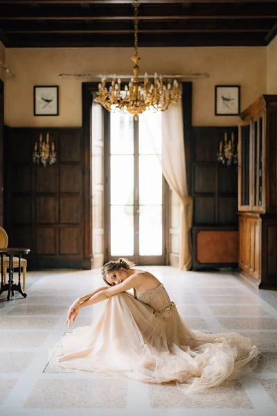 Noiva em um vestido bonito senta-se no chão da sala com a cabeça de joelhos contra o fundo da janela de uma antiga villa. Lago de Como — Fotografia de Stock