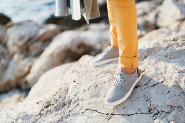 Spor ayakkabılı damadın ayakları denizin üzerindeki kayalık bir uçurumun arka planında bağlanmış.